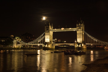 Tower bridge, full moon above, with river Thames illuminated in the night. London, United Kingdom