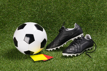 A soccer ball and boots on a green artificial turf with red and yellow cards for the judge - Powered by Adobe