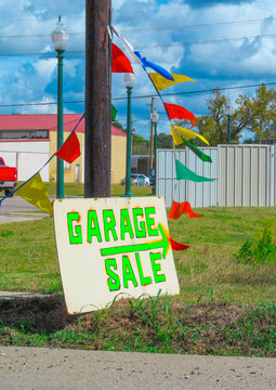 Self-made written painted sign GARAGE SALE with green letters and white background.
A hand made poster with arrow-pointer standing pinnacle on lawn next to the road.