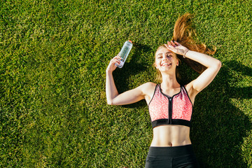 Portrait of a happy young fitness woman laughing and resting on grass after workout and smiling....