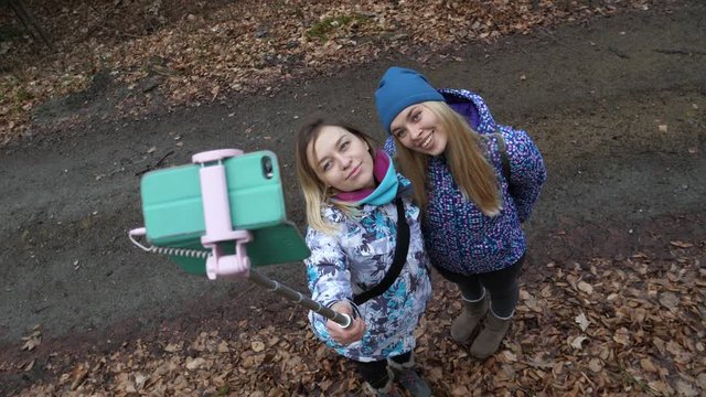 Cute blonde ladies girls friend hang out walking in forest enjoy taking selfie stick pictures