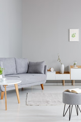 Simple, white and gray living room interior with a book on a stool, wooden table, cozy couch and cupboards. Real photo