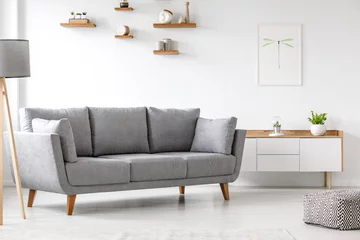 Foto op Plexiglas Simple, gray sofa standing next to a white cupboard in living room interior with decorations on wooden shelves. Real photo © Photographee.eu