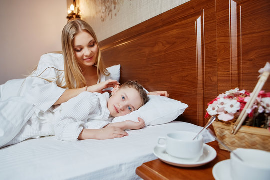 The loving mother irons the daughter lying in a bed on the head