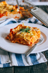 Traditional lasagna made with minced beef bolognese sauce topped with coriander leafs served on a white plate