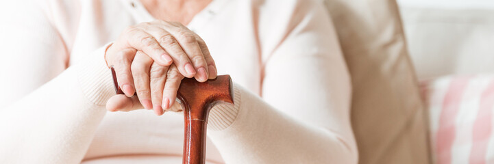 Close-up of senior woman's hands folded on a cane. Panorama.