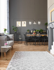 Grey carpet in spacious loft interior with sofa and black chairs at dining table under lamps. Real photo