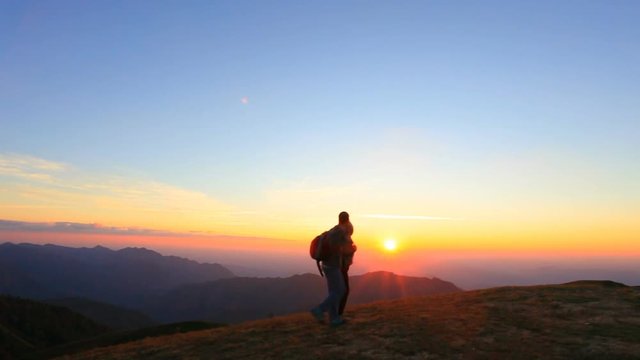 couple of hiker walking on top of mountain against beautiful sunset sky background