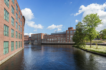 Old red brick industrial buildings along the Tammerkoski rapids in downtown Tampere, Finland on a sunny day.