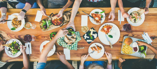 Family or friends summer party or outdoor dinner. Flat-lay of group of people at big table in cafe...