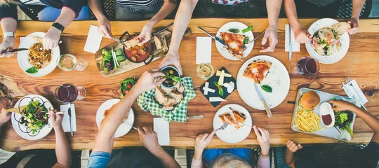 Fototapeten Family or friends summer party or outdoor dinner. Flat-lay of group of people at big table in cafe eating verious food together. Summer gathering or celebration concept © sonyakamoz
