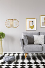Pillow placed on the checkerboard linoleum floor in grey sitting room interior with gold lamp,...
