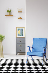 Open space room interior with linoleum checkerboard floor, blue armchair, fresh plants and poster...