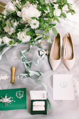 Elegant wedding bouquet with a ribbon, wedding invitation, rings and bridal shoes on tissue 