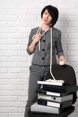 angry business woman with laptop and folders having stress, dressed in a gray suit poses in front of a white wall