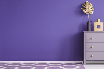 Purple empty wall in a room interior with a chest of drawers with vases and golden leaf, and...
