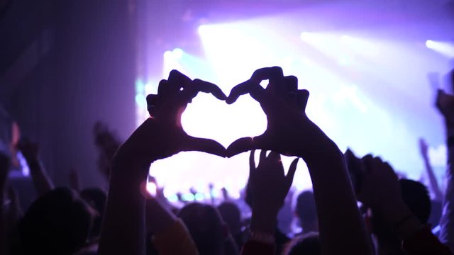Making heart silhouette young fan spectator girl fingers sway hand enjoy music concert in a crowd