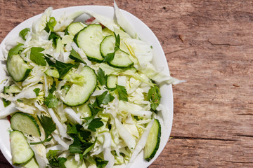 Spring vegan salad with cabbage, cucumber, green onion and parsley on wooden table. Top view