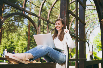 Obraz premium Young successful businesswoman in light casual clothes. Smiling Woman working on modern laptop pc computer in city park in street outdoors on spring nature. Mobile Office. Freelance business concept.