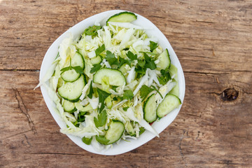 Spring vegan salad with cabbage, cucumber, green onion and parsley on wooden table. Top view