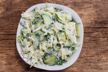 Spring salad with cabbage, cucumber, green onion, parsley and mayonnaise on wooden table
