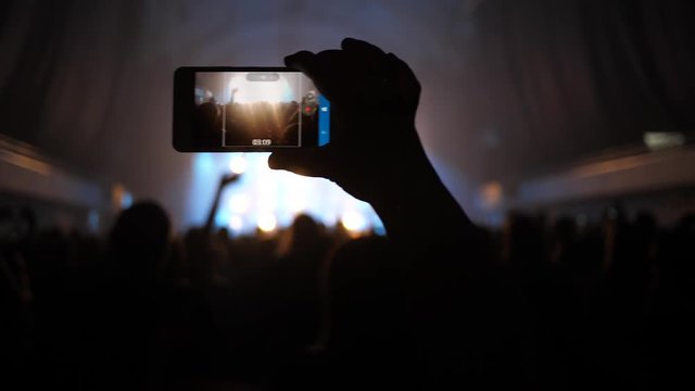 Spectator fan holding mobile smartphone shooting concert video staying in crowd