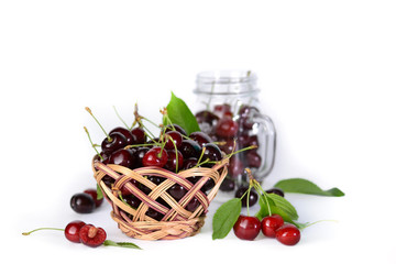 Basket with cherries and a square glass jar with handles with cherries on a white background.