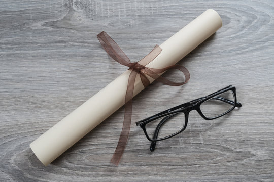 A Diploma Rolled Up And Tied With A Red Ribbon On The Table With A Pair Of Glasses
