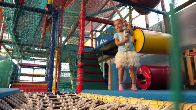 Kid girl fun jump swaying on the rope in amusement playground in restaurant