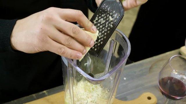 Male hands rubbing parmesan cheese on the metal grater for pesto sauce at cooking master class. 4K