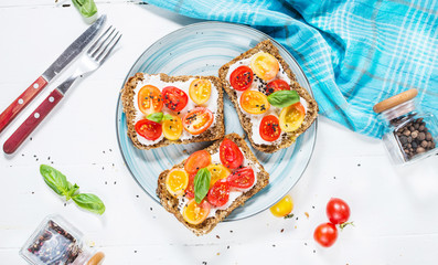 Sandwich with cream cheese, cherry tomatoes and basil on white wooden table
