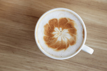 Cup of hot coffee with latte art on wooden background.