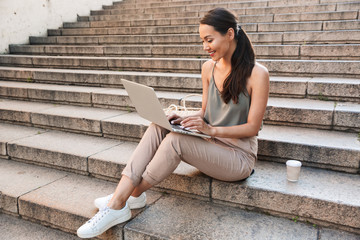 Photo of caucasian beautiful woman 20s wearing casual summer outfit, sitting on street stairs with...