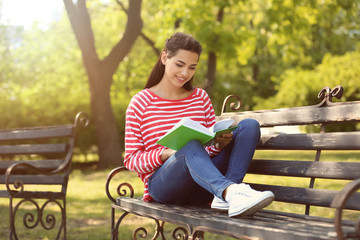 Beautiful young woman resting in park with book