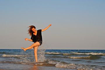 Beautiful woman wearing beach tunic having fun in water at the seaside at sunset