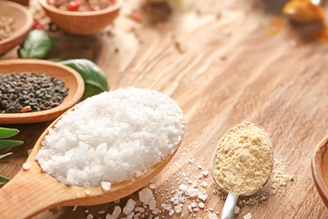 Spoons with salt and different spices on wooden table, closeup