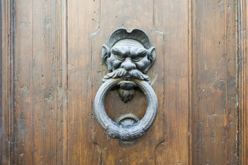 Old metal door handle in the form of a man head. Door knocker closeup background. Florence, Italy