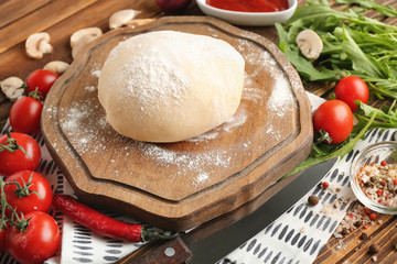 Composition with raw dough and ingredients for pizza on wooden background