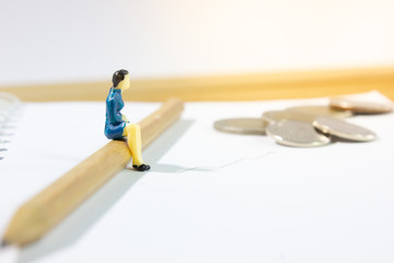 Miniature business women sitting on pencil with stationary background.