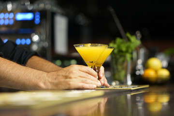 The barman gives a cocktail to the client of the hotel bar. Fresh cocktail with orange. Alcoholic, non-alcoholic drink-beverage at the bar counter in the night club. Glass of orange cocktail.