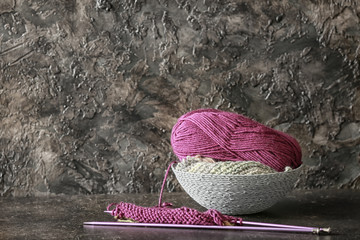Basket with knitting yarn and needles on table against dark textured background