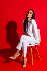 Posing snap portrait of cool hot woman in white suit sitting on chair looking at camera isolated on...