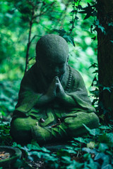 Fototapeta na wymiar Stone buddha statue in shadowy overgrown garden
