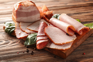 Wooden board with tasty sliced delicious meats on table