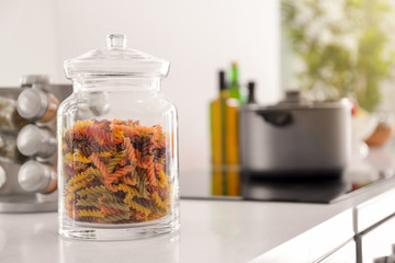 Jar with colorful raw pasta on table in kitchen