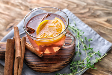 Cup of hot aromatic beverage with cinnamon and orange on wooden board