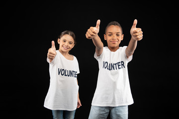 Well done. Joyful cute little volunteers wearing white shirts and showing their thumbs up