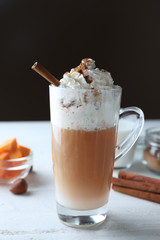 Glass cup of tasty latte with cinnamon on white table against dark background