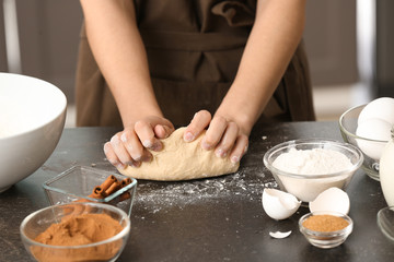 Obraz na płótnie Canvas Woman kneading dough for cinnamon buns at table