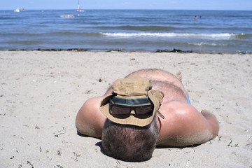 man sunbathes on the beach with a cap on the head